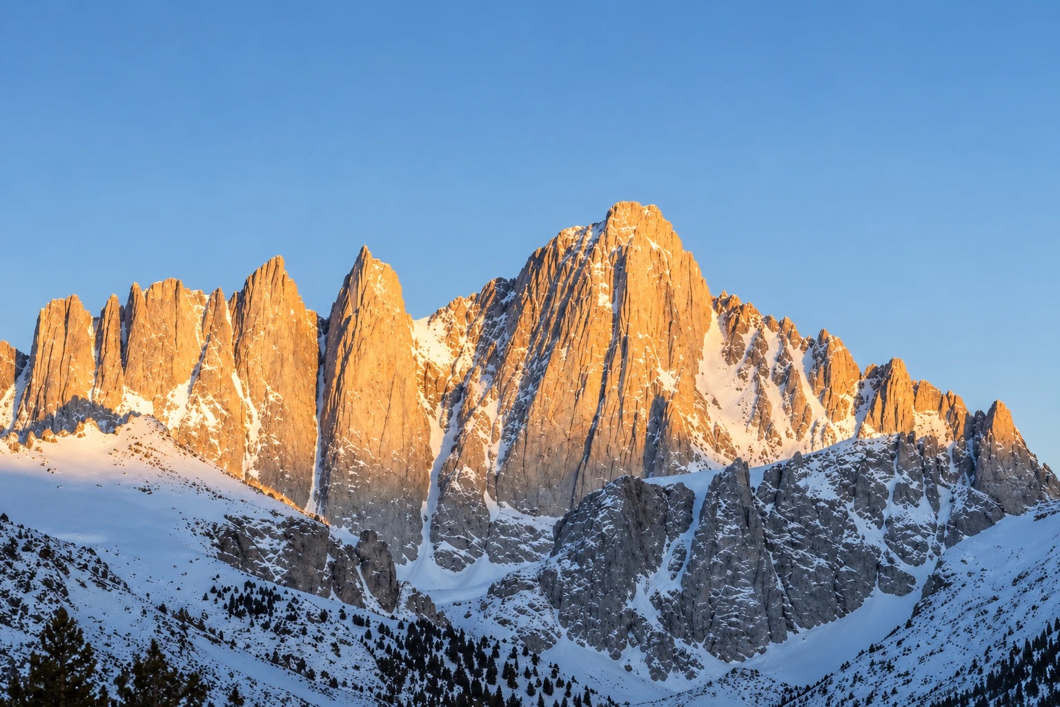 Mount Whitney's jagged granite spires lit orange by first light above snowy slopes